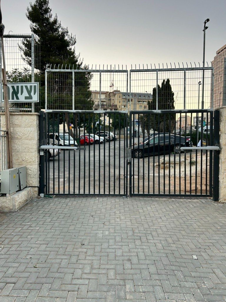 שער כנף חשמלי שחור עם מנועי זרוע בכניסת חניון | שפירא מערכות